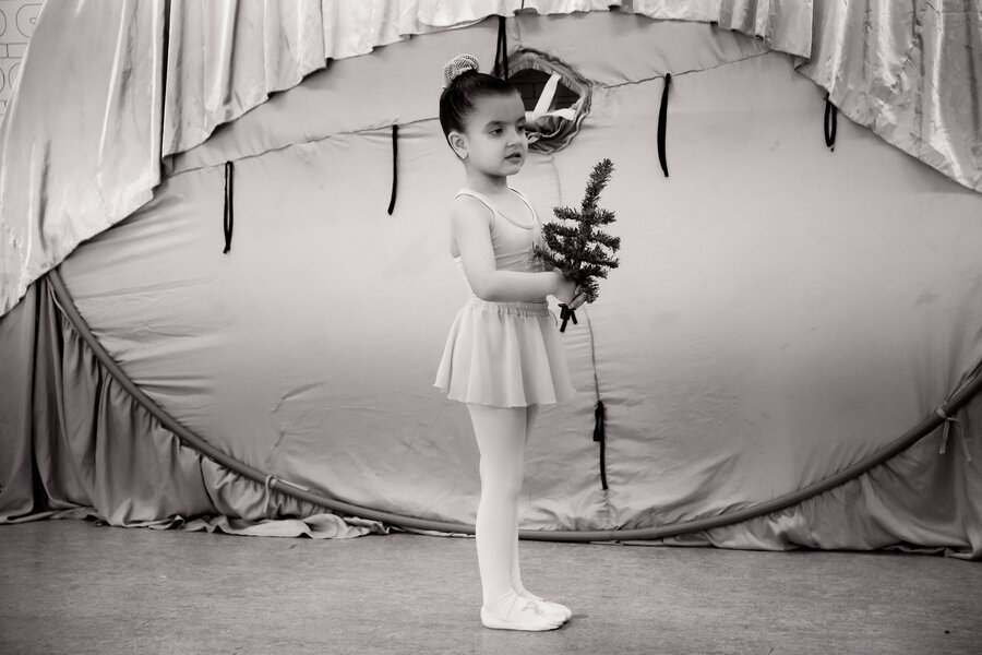 Bailarina em perfil segurando um galho de pinheiro, com cortina de palco ao fundo